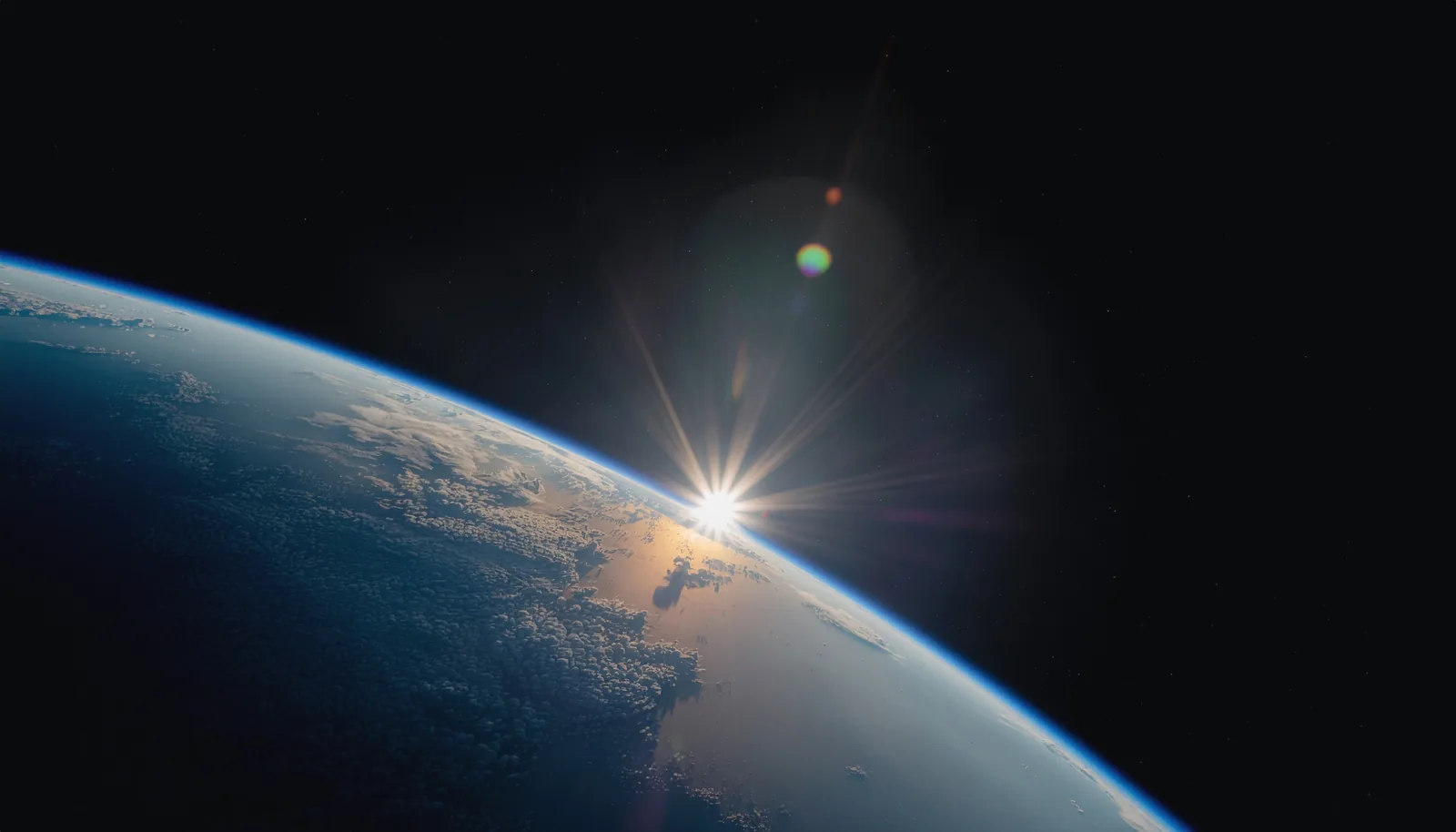 宇宙から見た地球の地平線。縁から太陽がのぞき、薄い大気の層が光る